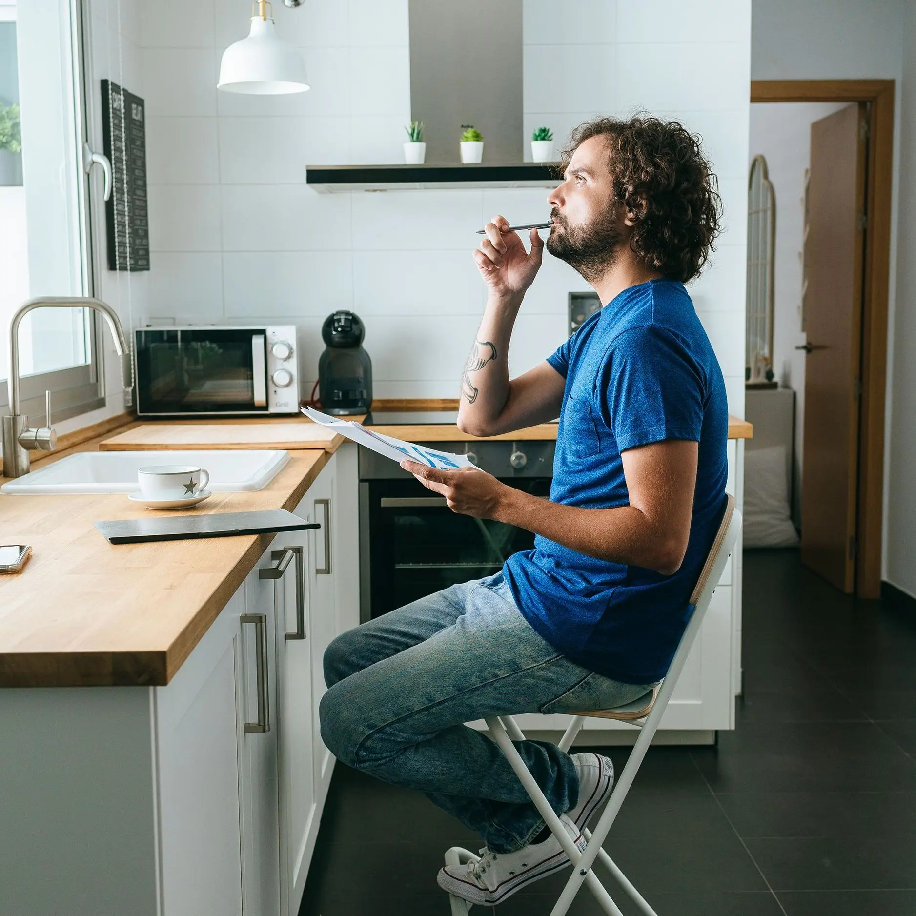 A man in a blue shirt sitting in his kitchen with several papers in hand