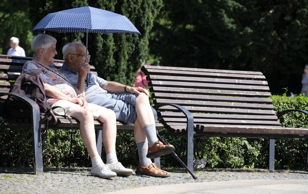 Two pensioners on a park bench with umbrella