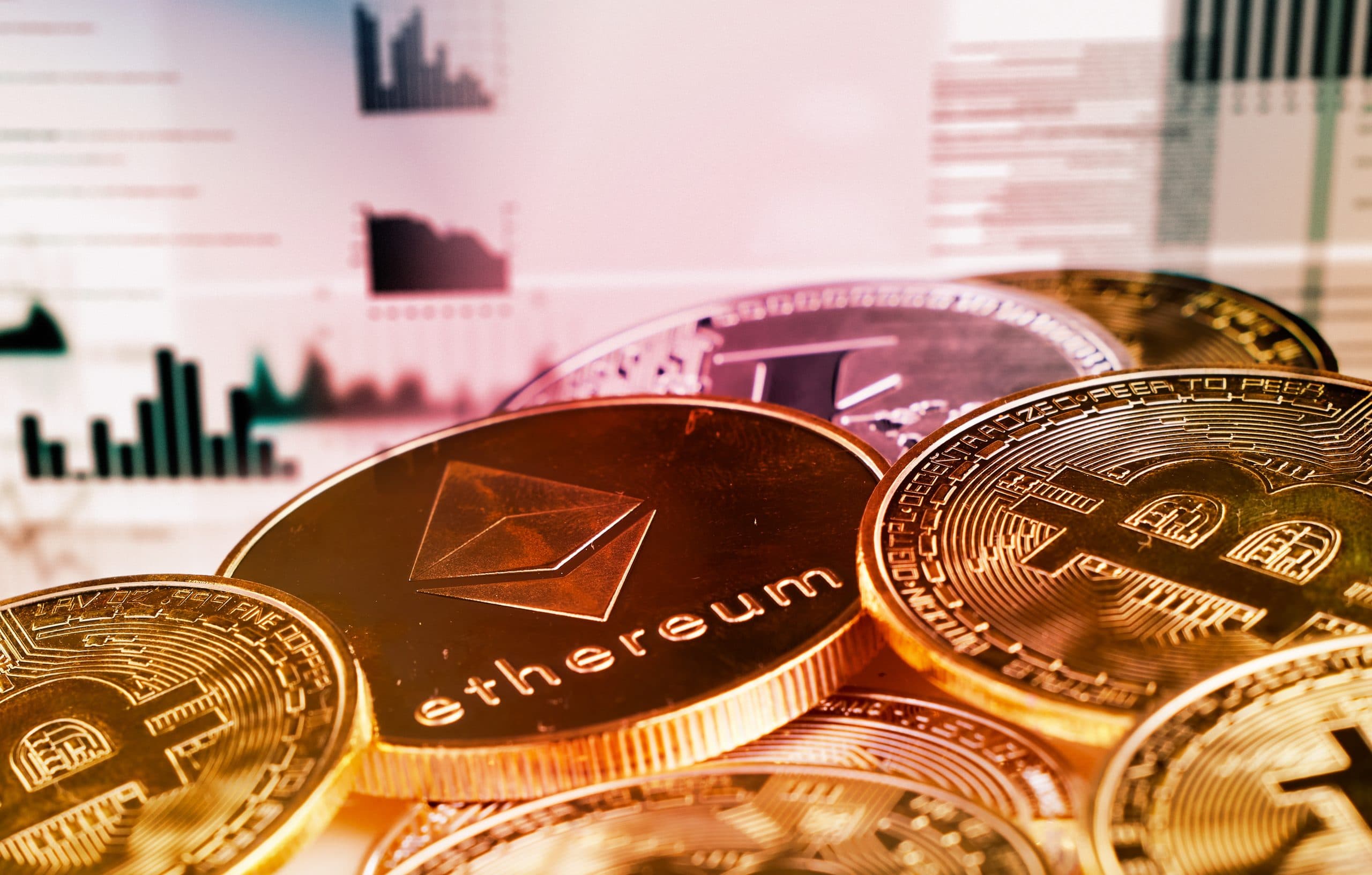 Multiple cryptocurrencies in coin form stacking against a background with charts