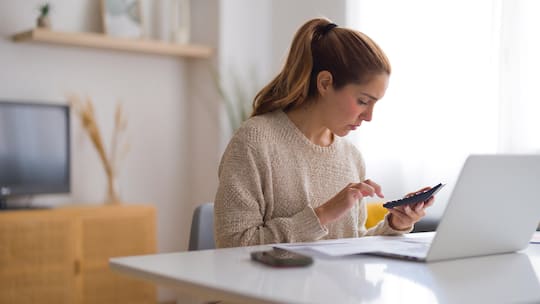 A woman sits at a laptop and types on a calculator, wondering if she knows