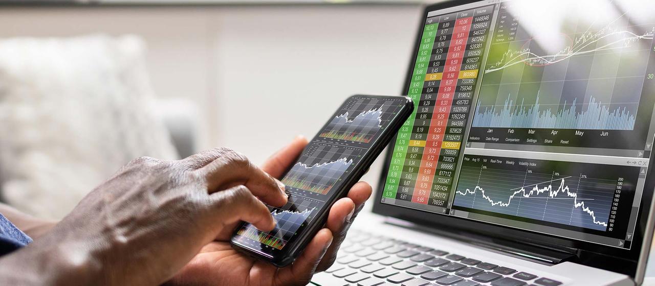 Person checking stock prices on smartphone and laptop