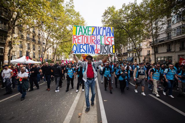 Een demonstrant met een bord dat pleit voor de „Taxe Zucman" in Parijs in oktober 2025.