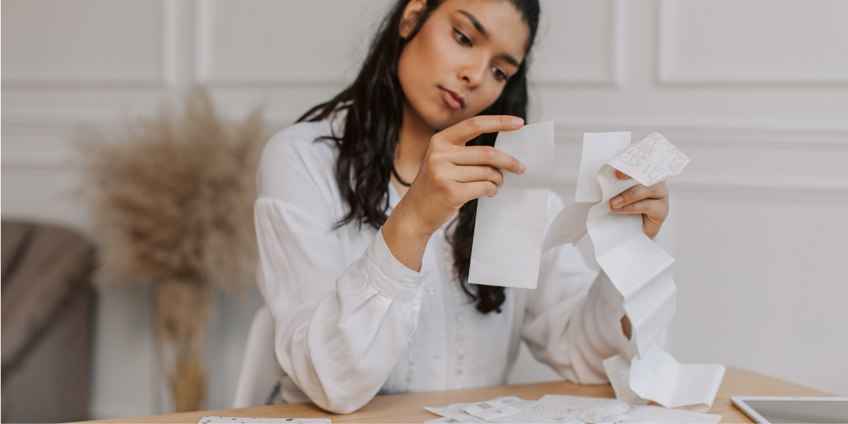 Frau prüft Kassenbons und Ausgaben am Tisch zu Hause