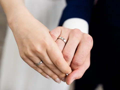Two hands holding wedding rings representing financial entanglement and debt