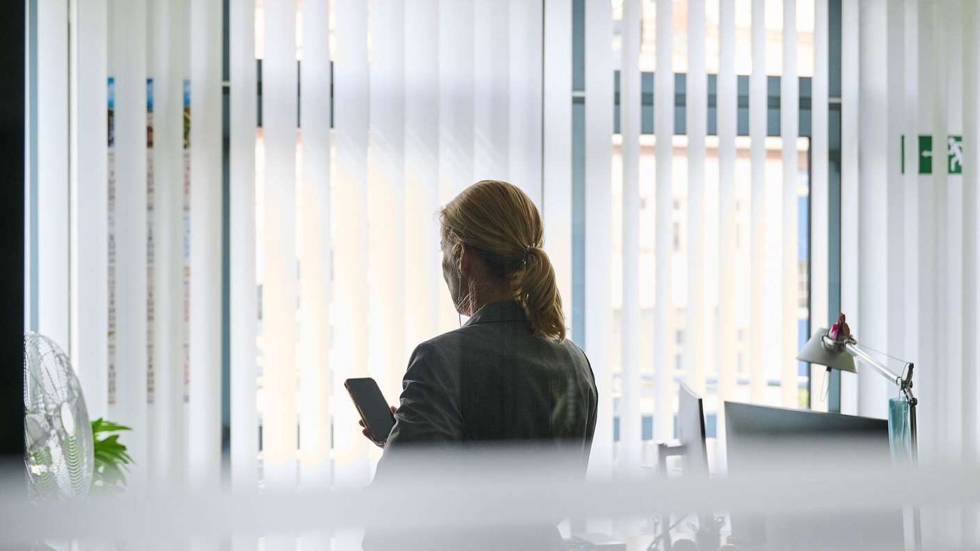 Frau steht in einem Bürozimmer am Fenster und telefoniert