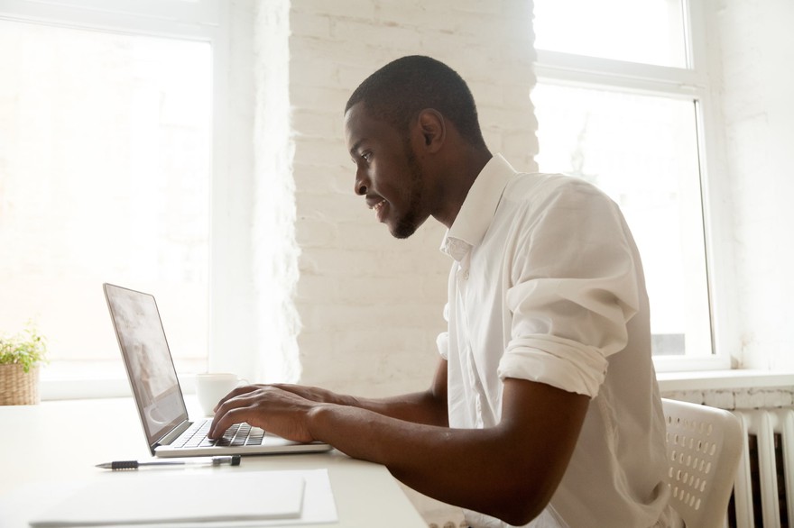 Businessman working on laptop sitting at home office desk analyzing investment portfolios